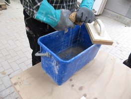 Hier ist zu sehen, wie ein Schwamm mit den Händen ausgewrungen wird. Dabei trägt die Person wasserdichte Handschuhe.