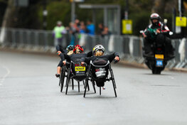 Auf einer abgesperrten Straße sind von hinten drei professionelle Teilnehmerinnen des Rollstuhl-Marathons in London zu sehen.