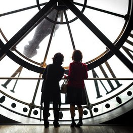 2 Kinder stehen vor einer großen Uhr.