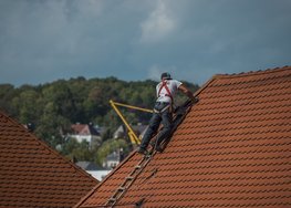 Hier ist ein Dachdecker bei der Arbeit auf einem Satteldach zu sehen.