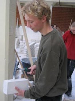 Das Bild zeigt einen Schüler, der einen KS- Stein mit einem Maurerhammer zurichtet.