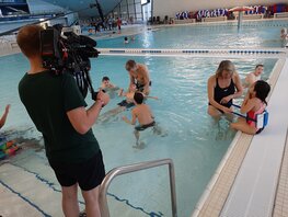 Ein Kameramann filmt zwei Lehrkräfte mit ihrer Gruppe beim Schwimmen.