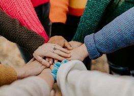 Menschen stehen im Kreis und legen ihre Hände aufeinander.