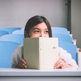 Die Augen eines fröhlichen Mädchens schauen über ein Buch hinweg. 