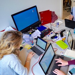 Gruppe von jungen Erwachenen, die an einem großen Tisch mit vielen Laptops sitzen.