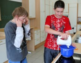 Auf diesem Bild sieht man einen Schüler der mit dem Handmixer arbeitet. Ein anderer hält sich die Ohren zu.