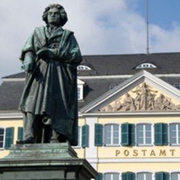 Vor der historischen Postamt-Fassade in Bonn steht ein Beethhoven-Denkmal.