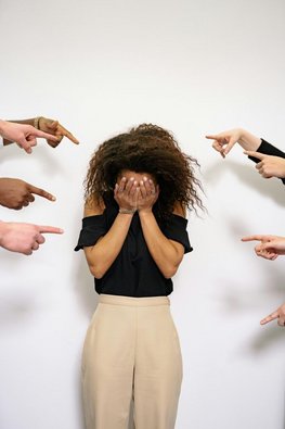 Eine Frau hält die Hände vor ihr Gesicht. Andere Finger zeigen auf Sie