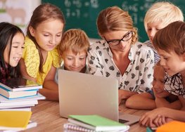 Lehrerin und Kinder schauen gemeinsam konzentriert auf Laptopbildschirm