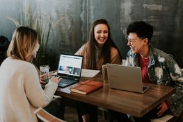 Lachende Leute mit Laptops um Tisch