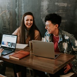 Lachende Leute mit Laptops um Tisch