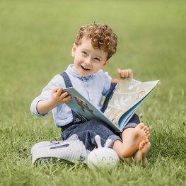 Ein Junge sitz auf der Wiese und halt ein Buch in der Hand