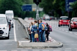 Auf einer Verkehrsinsel in der Mitte einer vierspurigen Straße drängeln sich mehrere Kinder.