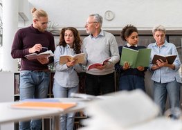 Fünf Erwachsene stehen nebeneinander und singen etwas vor.