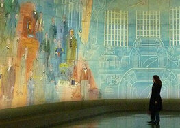 In einem großen Raum, dessen Wände vollständig mit einem Kunstwerk bemalt sind, steht eine einzelne Person im Gegenlicht.