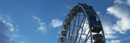 Der obere Teil eines Riesenrades vor blauem Himmel mit wenig weißen Wolken