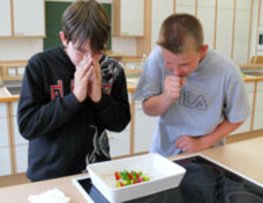 Zwei Schüler bereiten einen Salat zu. Dabei husten sie über die Salatschale.