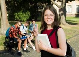 Junge Frau mit Schreibblock vor einer Gruppe Schüler auf einem Campus.